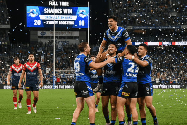 A group of Cronulla Sharks rugby league players in blue and white jerseys celebrate on the field as confetti falls around them.