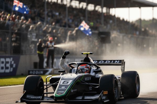 Alex Ninovic in his Rodin Motorsport car raises his fist in triumph on the track at Donington Park, with cheering crowds and Australian flags in the background.